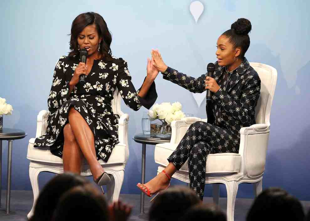 Michelle Obama and Yara Shahidi high fiving while sitting on white chairs on stage