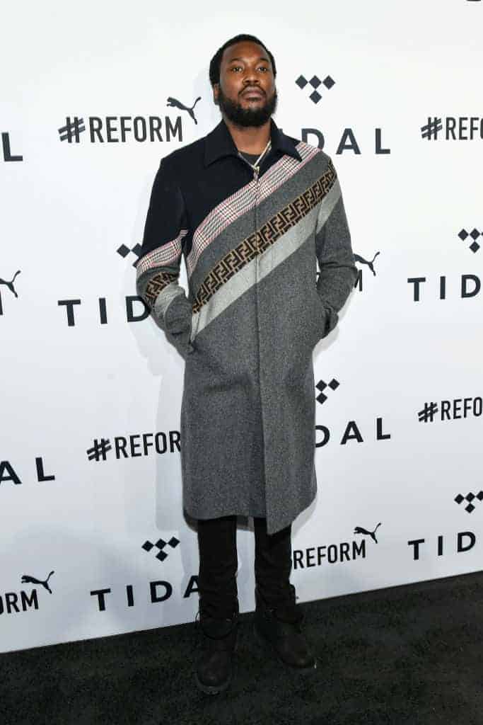 Meek Mill wearing Black and White standing in front of Tidal backdrop