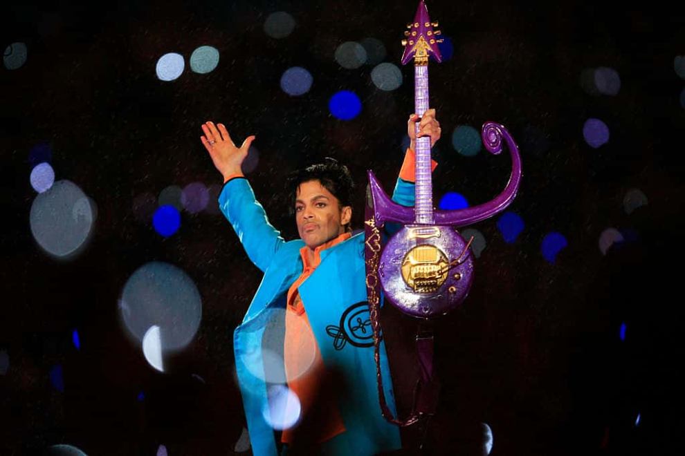 Prince on Stage wearing a Blue suit holding a Purple Guitar