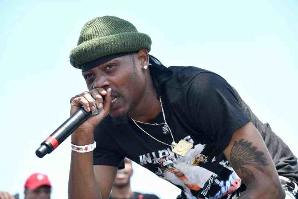 Flipp Dinero wearing a black shirt and green hat